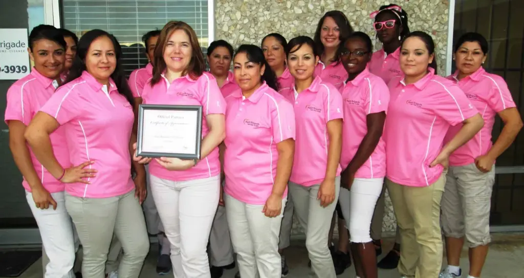 The DomesticAide team in pink uniforms holding a Cleaning for a Reason partner certificate