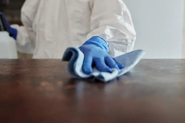 A gloved hand wiping a dark countertop with a blue microfibre cloth